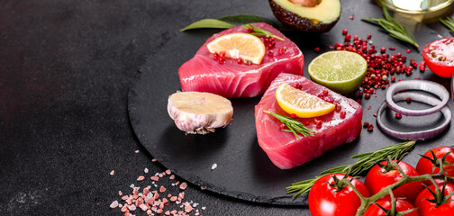 Fresh tuna fillet steaks with spices and herbs on a black background