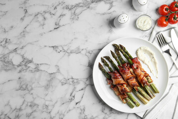 Oven baked asparagus wrapped with bacon on white marble table, flat lay. Space for text