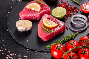 Fresh tuna fillet steaks with spices and herbs on a black background