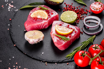 Fresh tuna fillet steaks with spices and herbs on a black background