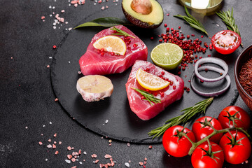 Fresh tuna fillet steaks with spices and herbs on a black background