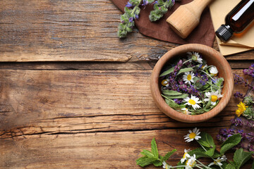 Flat lay composition with mortar and different healing herbs on wooden table, space for text