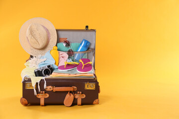 Packed vintage suitcase with different beach objects on orange background, space for text. Summer...
