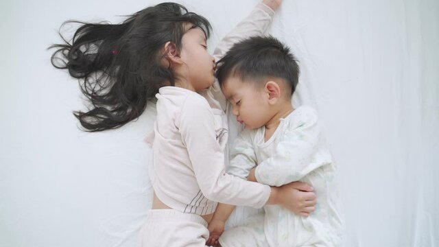 Asian sibling of sister and brother are sleeping together on the white bed in the morning time.