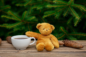 cup of coffee and teddy bear on wooden table with spruce branches on background