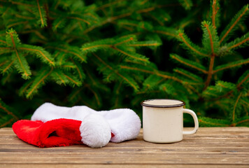 Obraz na płótnie Canvas cup of coffee and Santa Claus hat on wooden table with spruce branches on background