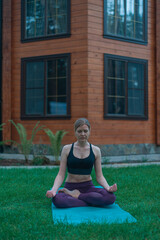 Young girl, woman practicing yoga on the lawn in front of her house. Outdoor yoga