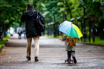 A little girl walks in the rain along the boulevard with a multi-colored broken umbrella