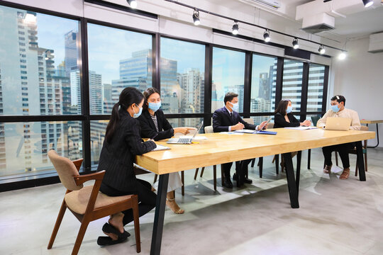 Asian people from various gender (gay, LGBT) working together in co-working space following social distancing and new normal by wearing facial mask in the business office workplace during covid-19
