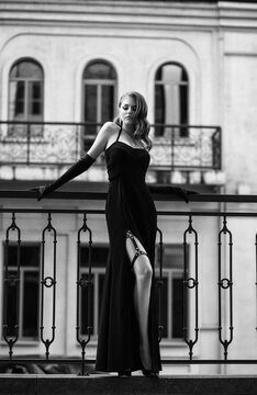 Sexy girl in classic evening dress. Black and white photo film. Luxury vintage woman. Beautiful Lady in retro image. Glamour queen Hollywood wave hair. Noir fashion model posing on balcony of Venice