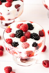 Delicious juicy berries of raspberries and blackberries with yoghurt in a glass form on a white background