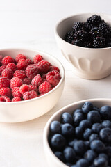 Raspberries, blueberries and blackberries close-up in bowls on a white background, ripe juicy berries
