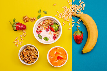 Healthy breakfast with granola and fruits, in white bowls, with a yellow and light blue background. 