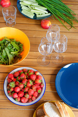 lunch in the country, fresh berries, lettuce, vegetables and green onions on a wooden table. Bright dishes on a wooden table. breakfast in nature