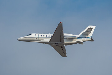 White small turbofan-powered business jet airplane flying in the air after takeoff from airport. Fast modern aircraft for air transportation. Aviation technology. Travel and business concept.