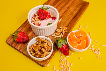 Healthy breakfast with granola and fruits on a wooden table, in white bowls, with a yellow background. 