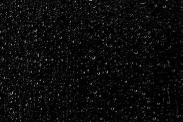 Drops of water flow down the surface of the clear glass on a black background. Texture for...