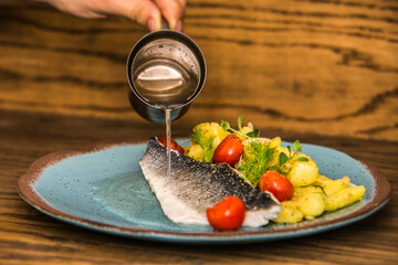 The chef in the kitchen prepares grilled fish fillet with fresh vegetables  served on plate. The food in the restaurant. Food styling and restaurant meal serving.