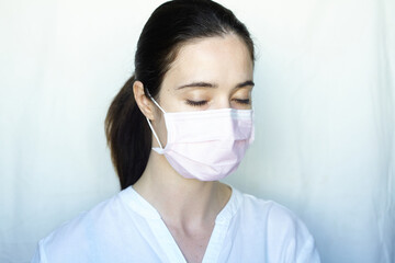 A woman in gloves and a protective mask stands on a light background in a white jacket. The concept of suppression of coronavirus