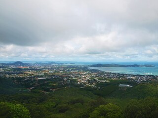Fototapeta na wymiar Panoramic view from the top to the bottom to the tropical coastal town. Sea harbour. Turquoise water and sky with gray cumulus clouds. Seascape. Islands, green forest, rainforest, jungle