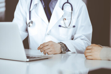 Unknown male doctor and patient woman discussing something while sitting in clinic and using laptop. Best medical service in hospital, medicine, pandemic stop