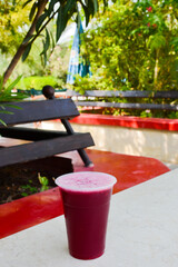 Red, freshly squeezed pomegranate juice in a plastic glass, in the park on the table. Vertical...