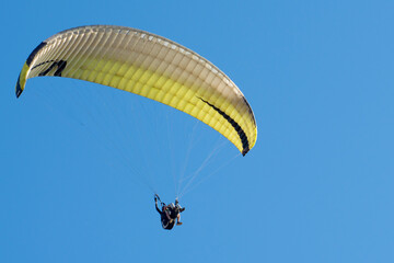 The wing of paraplan against a blue sky. Two paragliderists are flying in tandem. Copy space.