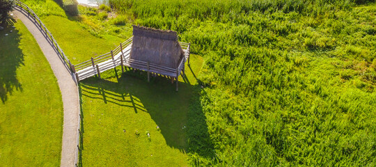 Fototapeta premium Ledro lake, Italy. Reconstructed huts on stilts to show the life during the prehistoric time. View of the lake and archeological area. An Unesco world heritage site
