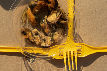 Bright yellow plastic forks on cardboard casts an overlapping shadow, next to a plate and oysters
