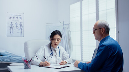 Female doctor recomending pills in her office to elderly retired senior man. Modern hospital or private clinic healthcare checkup for disease prevention and healthcare problems. Patient complaints and