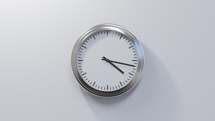 Glossy chrome clock on a white wall at seventeen past four. Time is 04:17 or 16:17