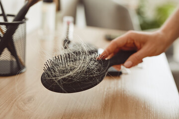 Close up of female hand holding brush full of hair, hair loss and alopecia concept, copy space