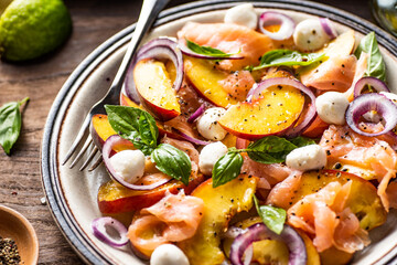 Refreshing summer salad with smoked salmon, peaches, mozzarella, red onion and basil. Wooden background.