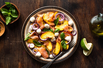 Refreshing summer salad with smoked salmon, peaches, mozzarella, red onion and basil. Wooden background.