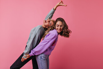 Excited white girls holding hands during funny dance. Studio shot of carefree female friends enjoying leisure time.