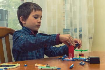 The boy playing an electric constructor. The child is played by intellectual toys. A boy in a blue shirt masters electronics. The concept of early development of children. toned