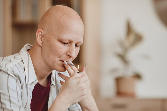 Warm-toned portrait of bald adult woman smoking marijuana joint for medicinal purposes in cancer recovery, copy space