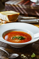 Tomato soup with fresh basil and grated cheese. Rustic table background.