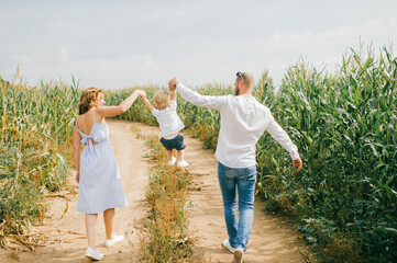 Cheerful family of three have a lot of fun together in the big cornfield in hot summer morning