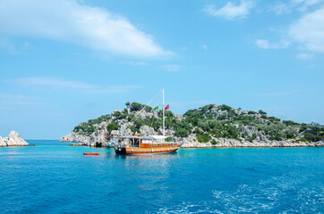 Obraz premium Tourist ship on the background of a beautiful summer mountain landscape on the Mediterranean sea. Excursion to Turkey. Sea tour of the historical monument of architecture. People on vacation