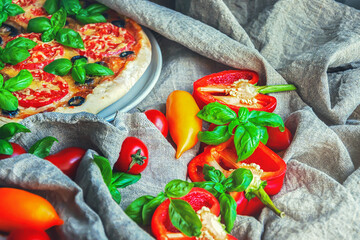 A fragment of Italian pizza,basil leaves and vegetables on a background of linen fabric, selective focus.