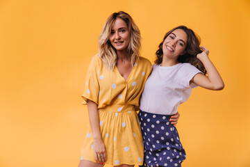 Inspired lady in yellow attire posing with her sister. Indoor shot of enthusiastic female friends...