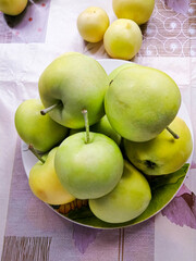 Green apples from the garden are in a plate on the table.
