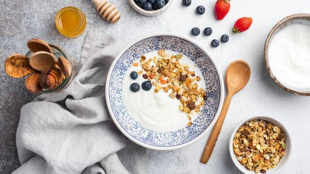 Stop motion animation of yogurt with granola and berries. Eating greek yogurt with crunchy oat honey granola, blueberries, strawberries and pomegranate seeds. Healthy food concept