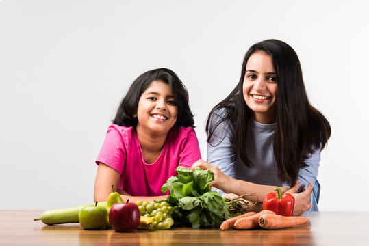 Happy Indian Family In The Kitchen. Pretty Mother & Cute Daughter Posing With Vegetables And Fruits