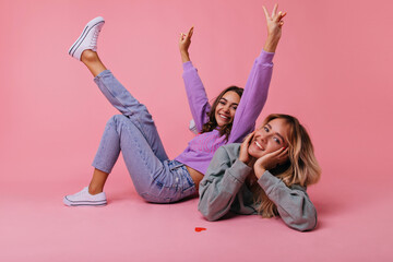 Excited girls in casual spring outfit posing on the floor. Positive best friends fooling around on...