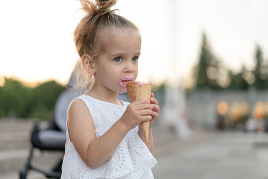 Little caucasian girl 3 years old eats ice cream closeup portrait