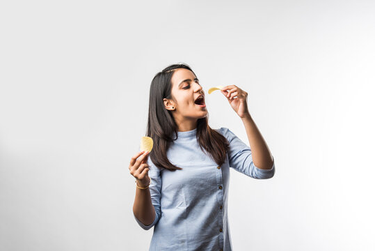 Indian / asian pretty young girl eating potato chips on white background with copyspace