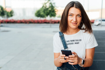 Portrait of a girl looking at a smiling camera holding a mobile phone in her hands.