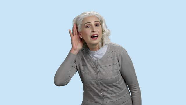 Curious senior woman holding hand near ear. Mature caucasian woman holds hand near ear and listen carefully on color background. Concept of eavesdropping.